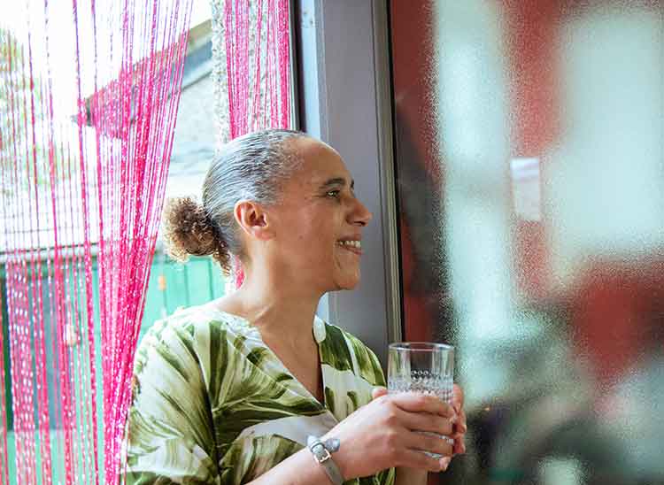 Aneita wearing a green plant print top and holding a glass of water and smiling