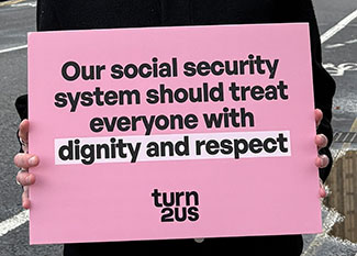 Turn2us employee holding placard with words 'our social security system should treat everyone with dignity and respect'