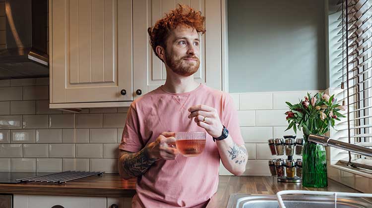 Man with red hair smiling and holding tea cup in his kitchen 