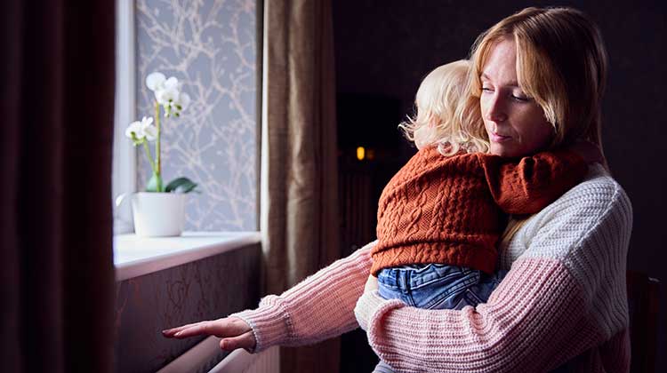 Mother cuddling child and holding hand over radiator