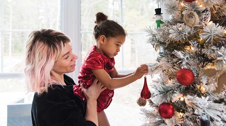 Woman with blonde and pink hair helping child decorate a Christmas tree