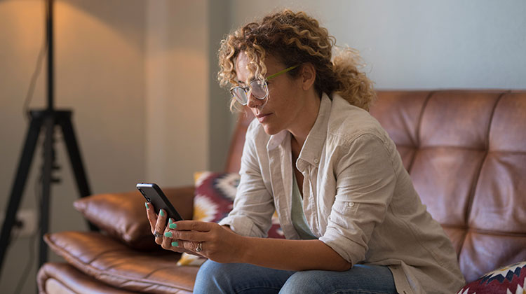 Woman with curly hair in a ponytail sitting on a sofa and looking at a phone