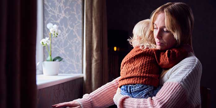 Mother standing near radiator to keep warm and holding her toddler