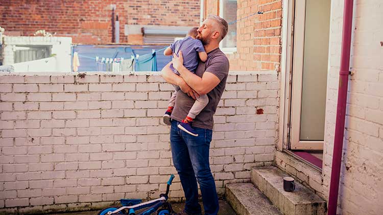 Man wearing t-shirt standing outside his house and holding his child
