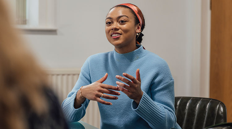 Smiling woman wearing light blue jumper talking to another woman