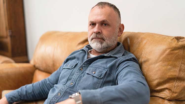 Man with grey hair wearing denim shirt - sitting on a brown sofa