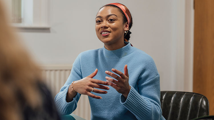 Woman wearing light blue jumper smiling and talking to another person