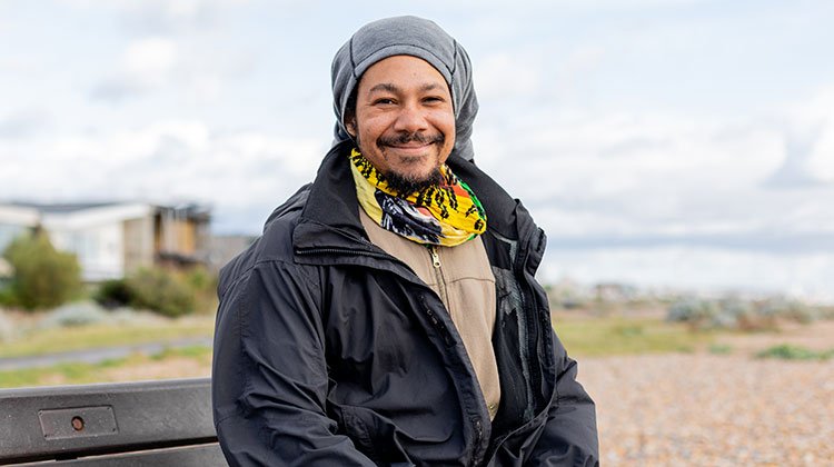 Smiling man in black anorak sitting on bench by beach