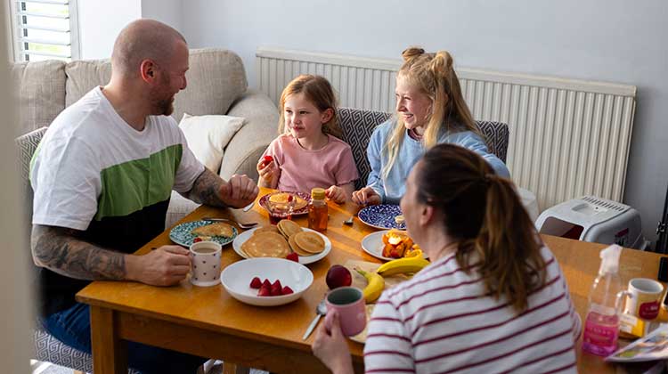 Family of four sat round a table eating a meal and chatting
