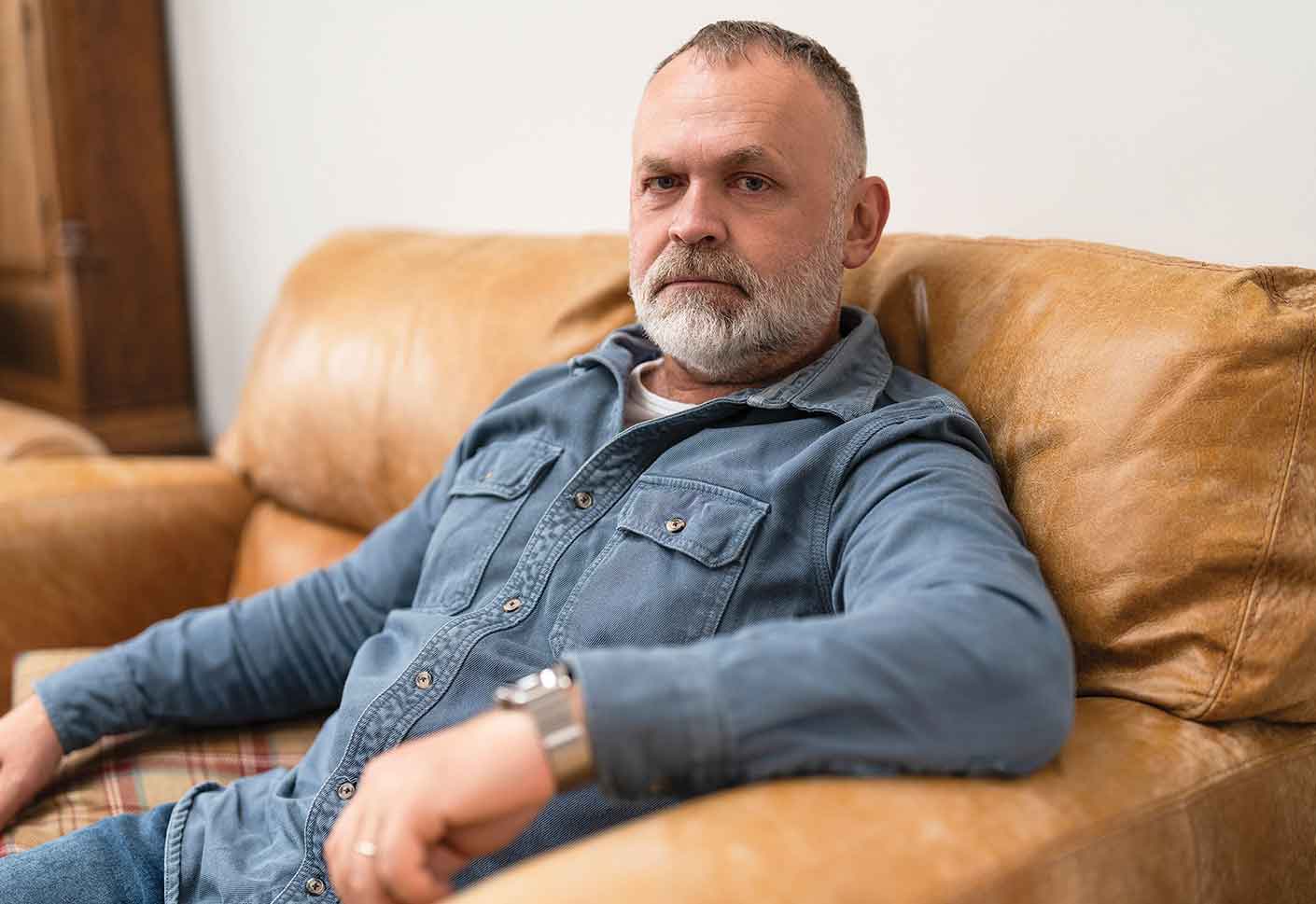 Man with grey hair wearing denim shirt - sitting on a brown sofa