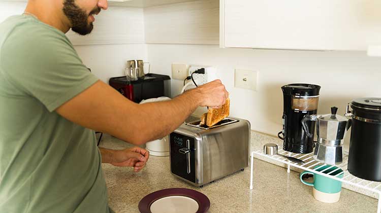 Man with beard wearing green t-shirt and putting toast in toaster