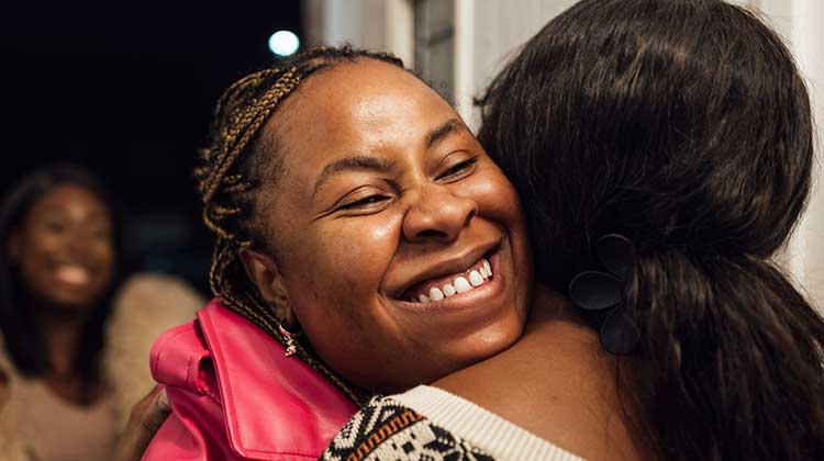 Smiling woman wearing pink coat hugging another woman