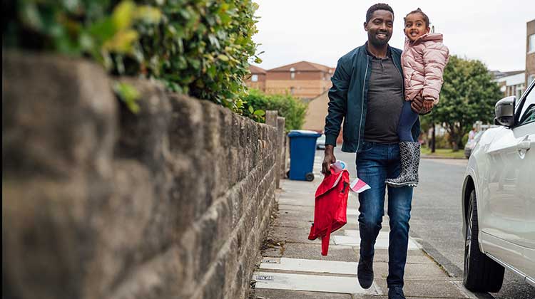Father carrying his daughter and her school bag along the street