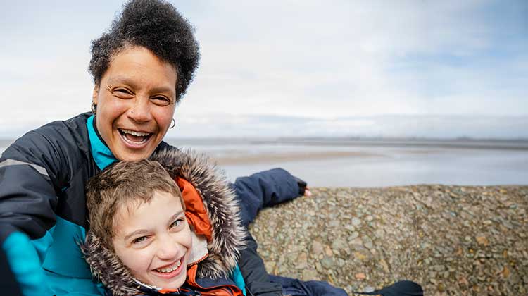 Mother holding child with sea and beach behind them