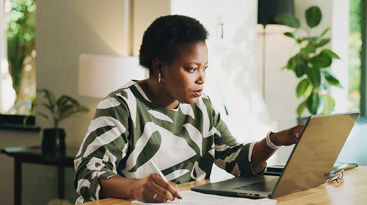 Woman wearing leaf patterned top making calculations at laptop