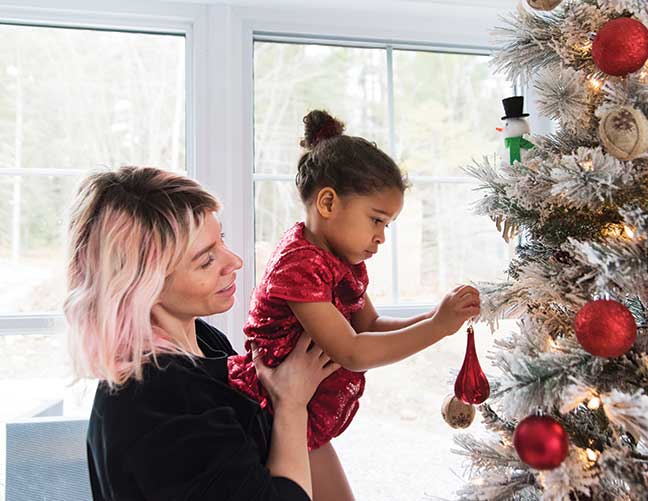 Woman with pink and blond hair helping child decorate a Christmas tree