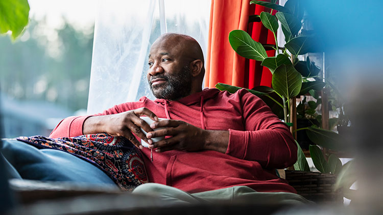 Man wearing red jumper sitting on a sofa looking out of the window