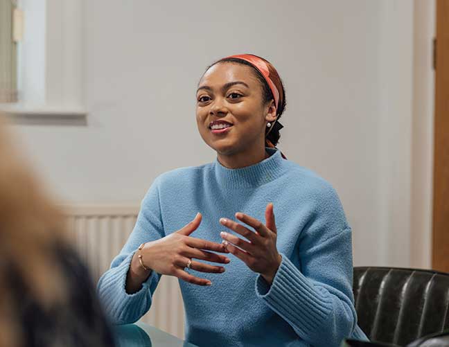 Woman wearing blue jumper smiling and talking to another person