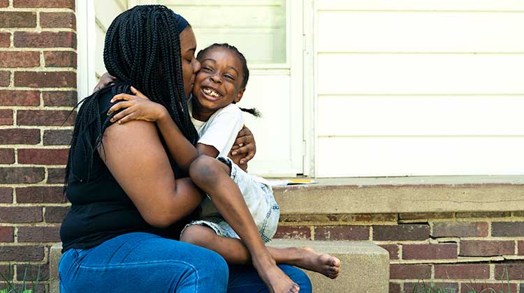 Mother hugging her daughter outside their property