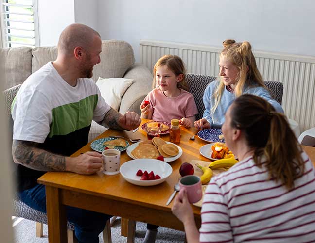 Family of four sat round table eating dinner and chatting