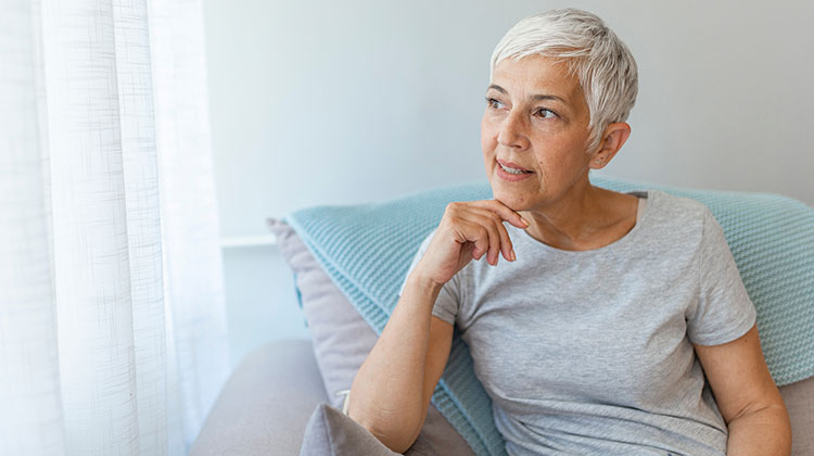 Woman with short grey hair sitting in an armchair and smiling by her window
