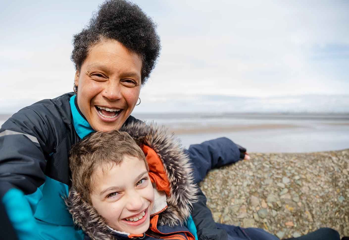 Mother with arms around her son by seaside - both smiling
